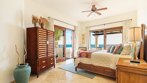 A bedroom with a bed, a dresser, a vanity, and a large window with a view of the ocean. - C301 Oceanview Penthouse with infinity pool and jacuzzi (San Jose del Cabo)