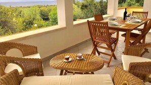 A covered outdoor dining area with wicker furniture and a table set for two, overlooking a scenic landscape.