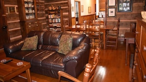 A log cabin interior with a leather sofa, wooden dining table, and a bookshelf. - 1850s log cabin 1 mile to downtown Weaverville 15% discount 7 days or more (Weaverville)