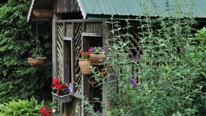 A rustic wooden structure with a green roof, surrounded by lush greenery and potted plants. - 1850s log cabin 1 mile to downtown Weaverville 15% discount 7 days or more (Weaverville)