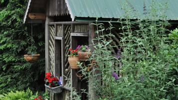 Une construction rustique en bois, surmontée d’un toit végétalisé, entourée d’une végétation luxuriante et de plantes en pot.