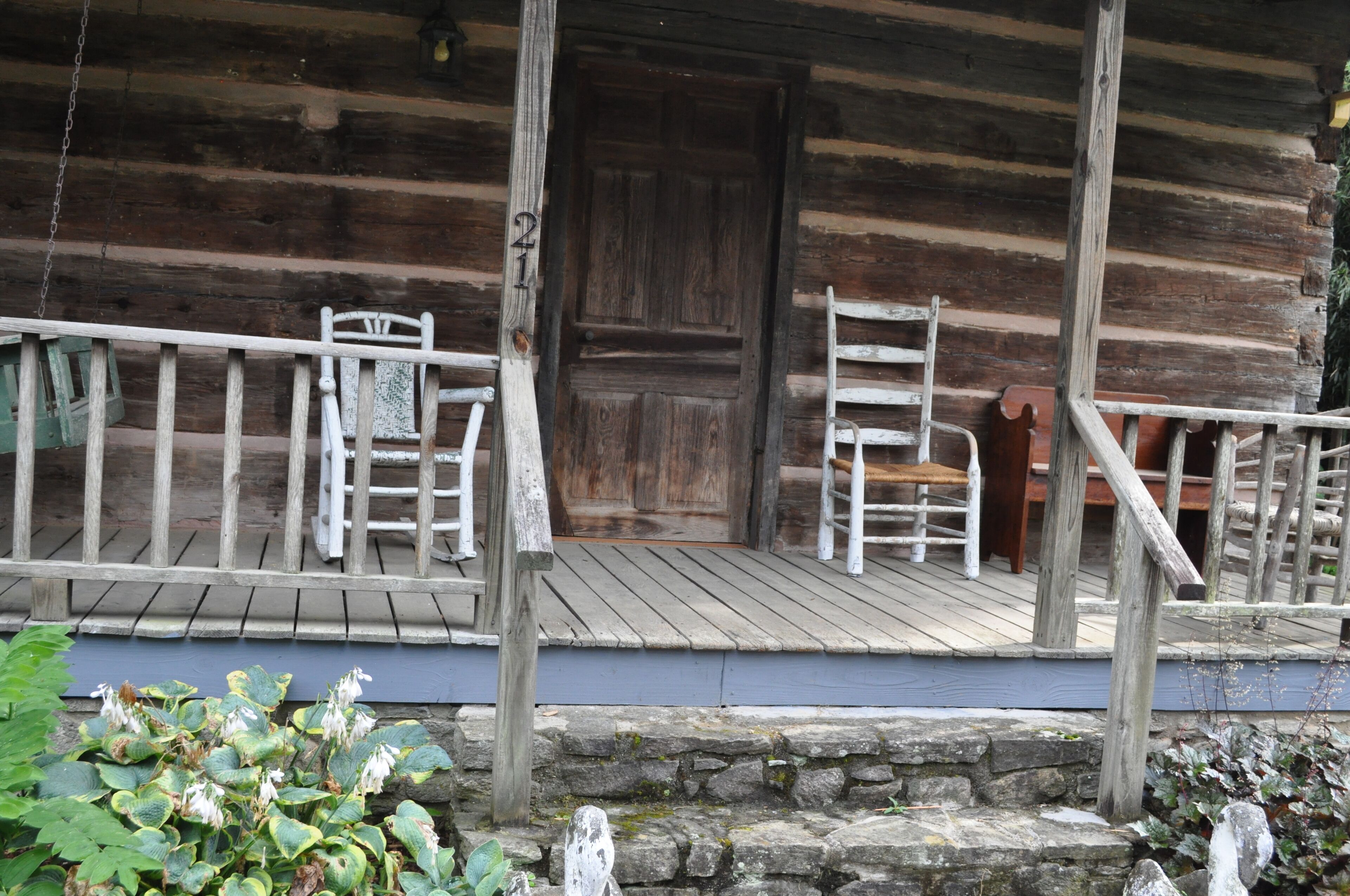 Une cabane en bois rustique, dotée d’un porche, d’une porte en bois et d’un mur en pierre.