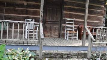 Une cabane en bois rustique, dotée d’un porche, d’une porte en bois et d’un mur en pierre.