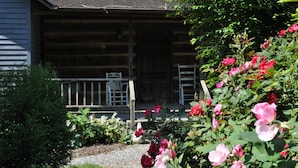 A rustic cabin with a wooden porch and a garden with blooming roses. - 1850s log cabin 1 mile to downtown Weaverville 15% discount 7 days or more (Weaverville)