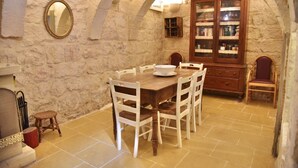 Un coin repas aux murs de pierre, avec une table en bois et des chaises blanches, un buffet aux portes vitrées et un miroir accroché au mur.