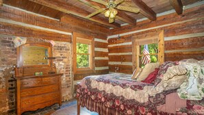 A log cabin bedroom with a wooden dresser, a bed with floral bedding, and a ceiling fan.