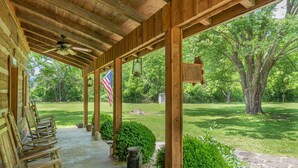A covered porch with wooden benches, an American flag, and a view of a grassy yard with trees.