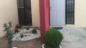 A house with a red door, a black window, and a small garden with white pebbles and plants. - La Casita Salesiana Aguascalientes (Aguascalientes)