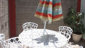 A round white metal table with a striped umbrella, a potted plant, and a brick wall. - La Casita Salesiana Aguascalientes (Aguascalientes)