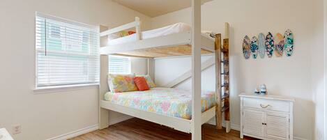 A bunk bed room with a window, a small white dresser, and a wall with decorative items.