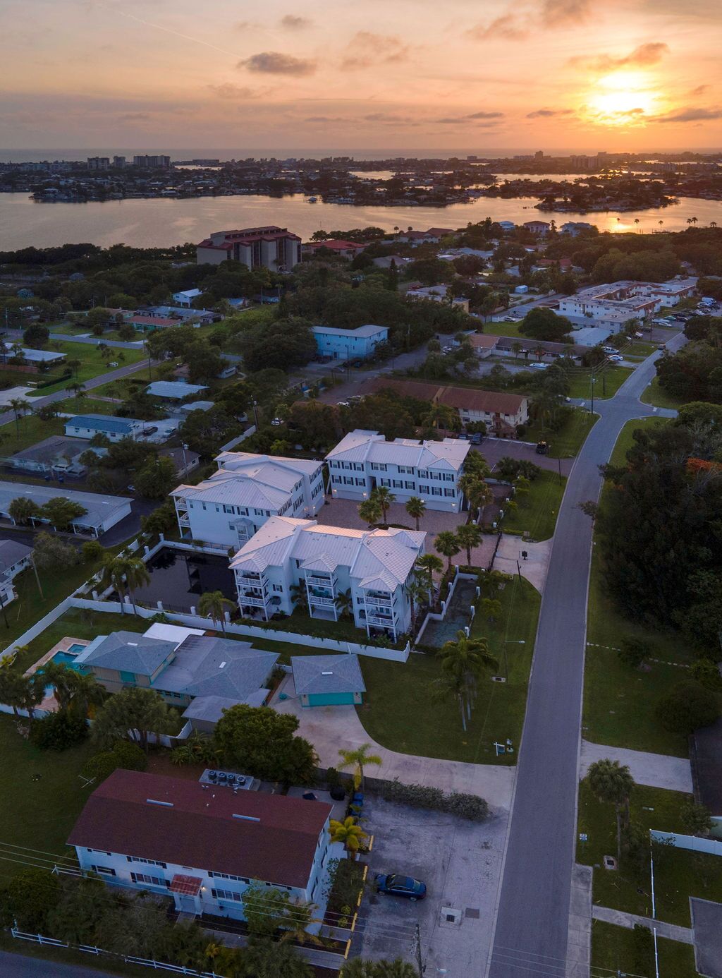 Vue aérienne d’un quartier résidentiel avec un grand ensemble de bâtiments blancs, une marina et un coucher de soleil en arrière-plan.