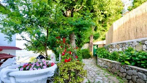 A stone pathway leading to a white wrought iron bench surrounded by lush greenery and flowering plants. - Belvedere Apt (Sorrento)