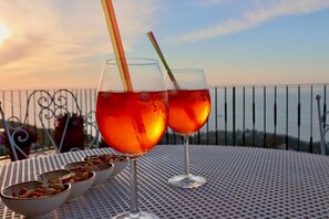 Two glasses of red beverage on a metal table with bowls of nuts, set against a balcony railing with a view. - Belvedere Apt (Sorrento)