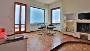 A living room with a sofa, a coffee table, a TV, and a fireplace. There are two windows and a door. - Belvedere Apt (Sorrento)