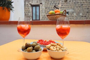 Une table avec deux verres d’une boisson rouge, des bols d’olives et de noix, et une assiette de tomates coupées en tranches.