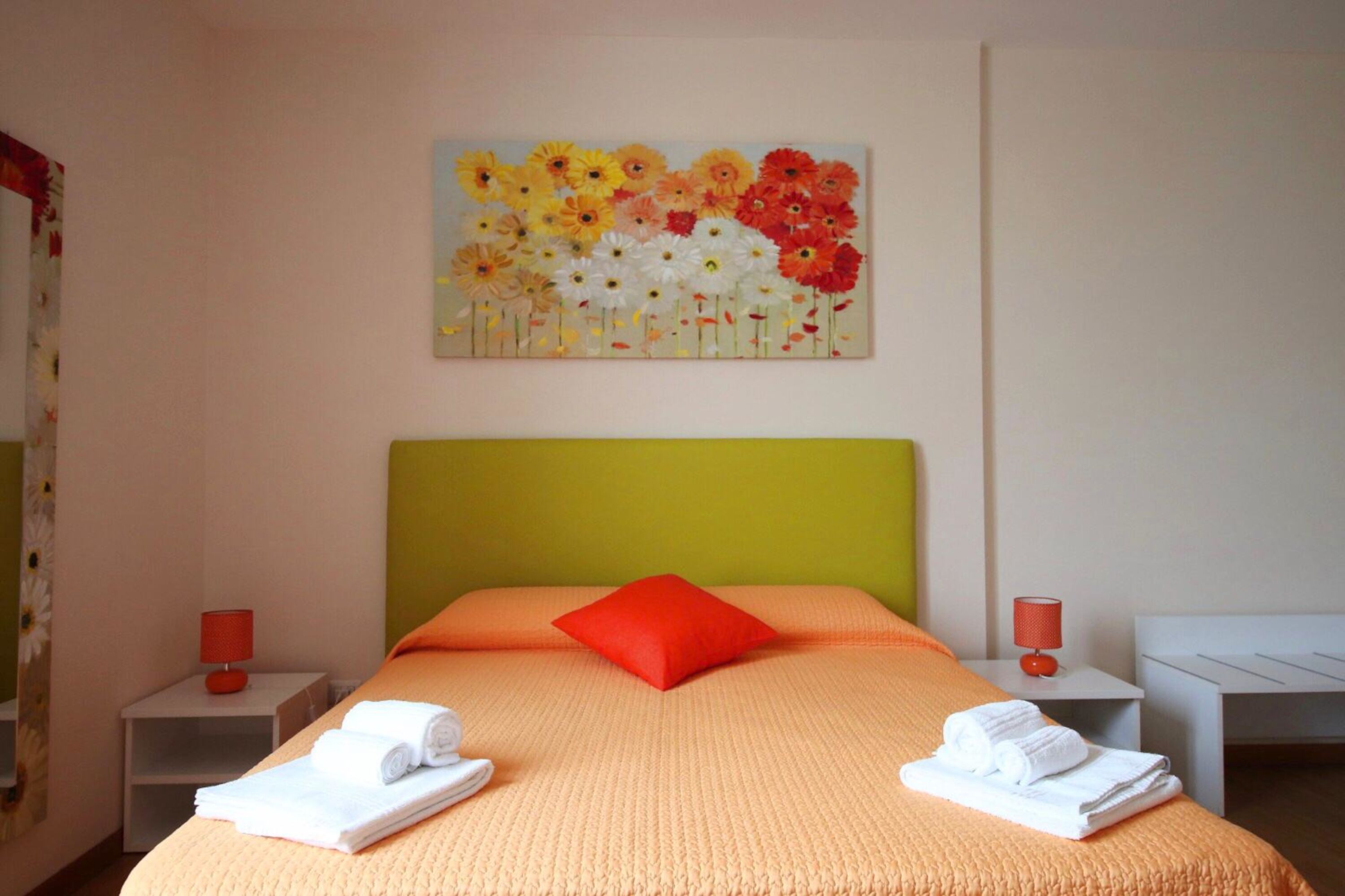A hotel room with a bed, a nightstand, a lamp, and a painting of flowers on the wall.