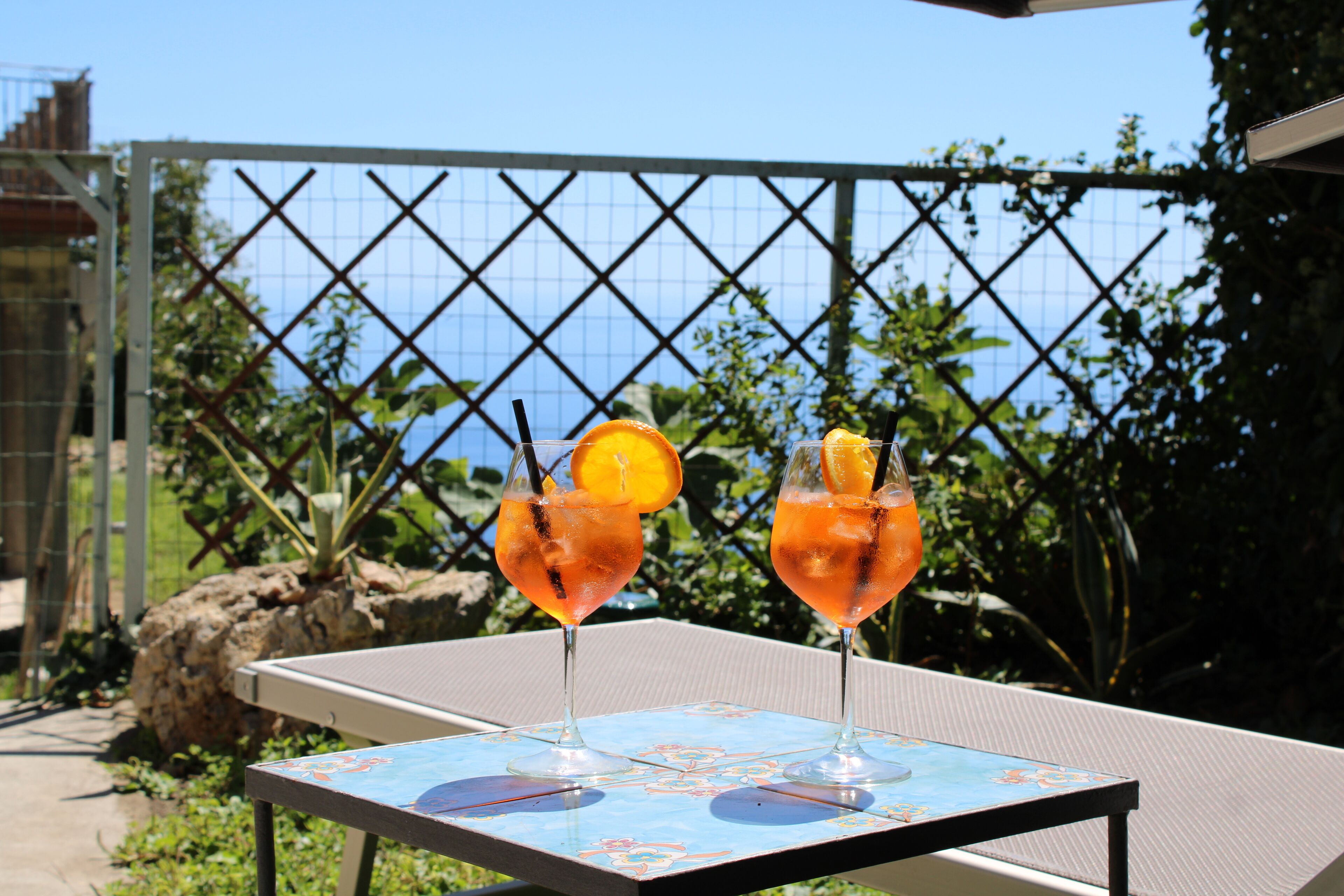 Deux boissons sur une table, avec une vue sur la mer et une clôture en arrière-plan.