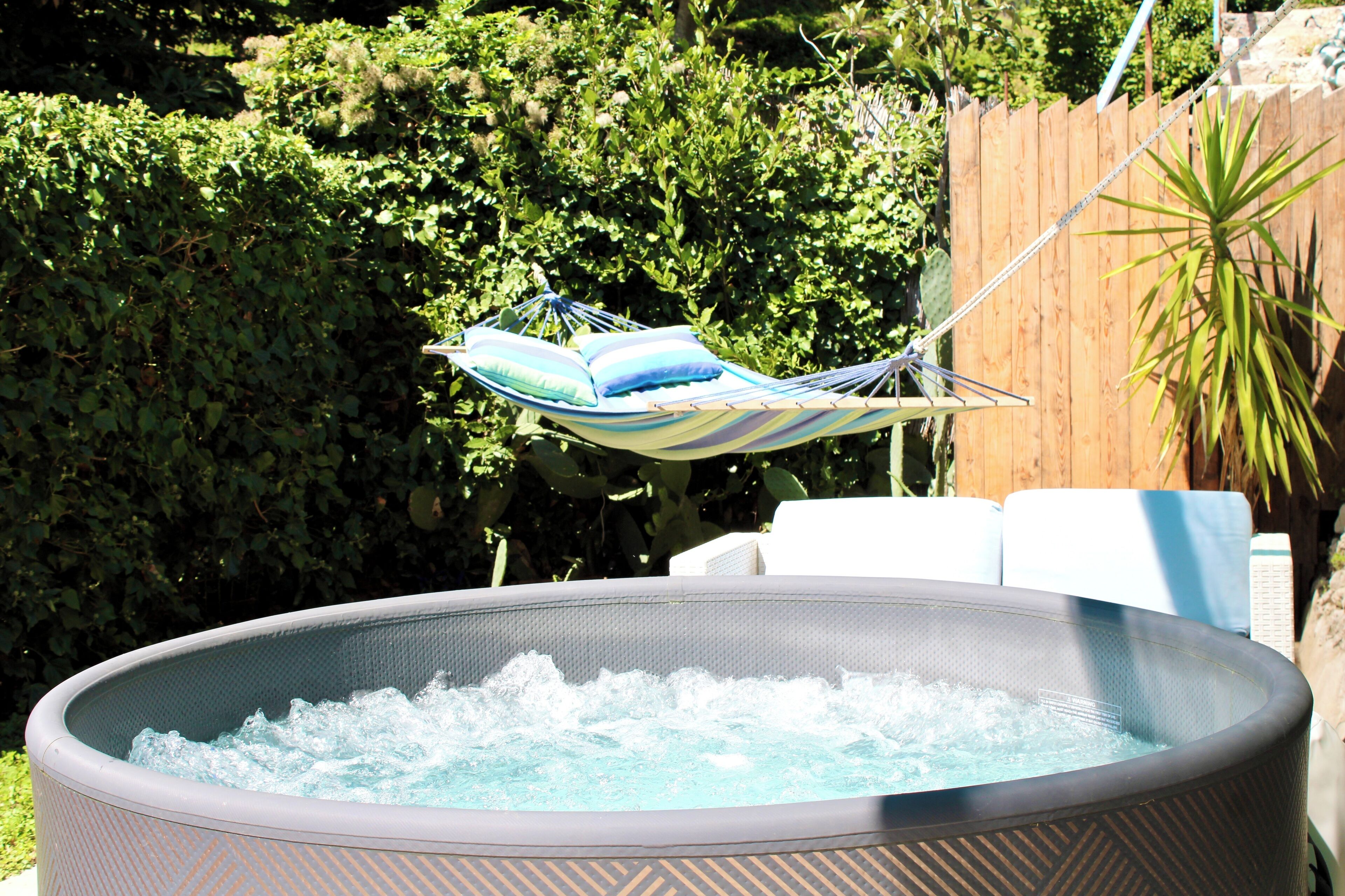 Un bain à remous équipé d’un fauteuil suspendu, entouré d’une végétation luxuriante et délimité par une clôture en bois.