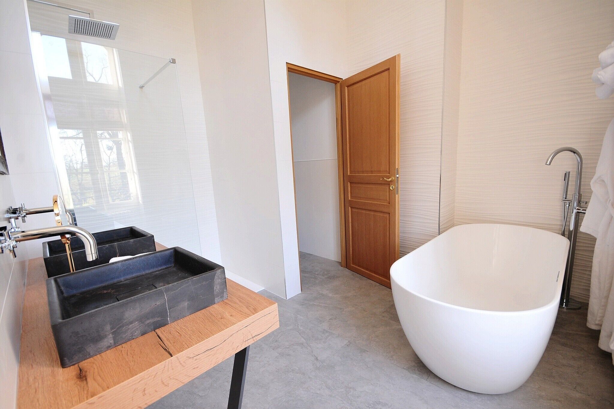 Un baño moderno con una bañera grande, un mueble de tocador de madera con un lavamanos negro y una puerta de madera.
