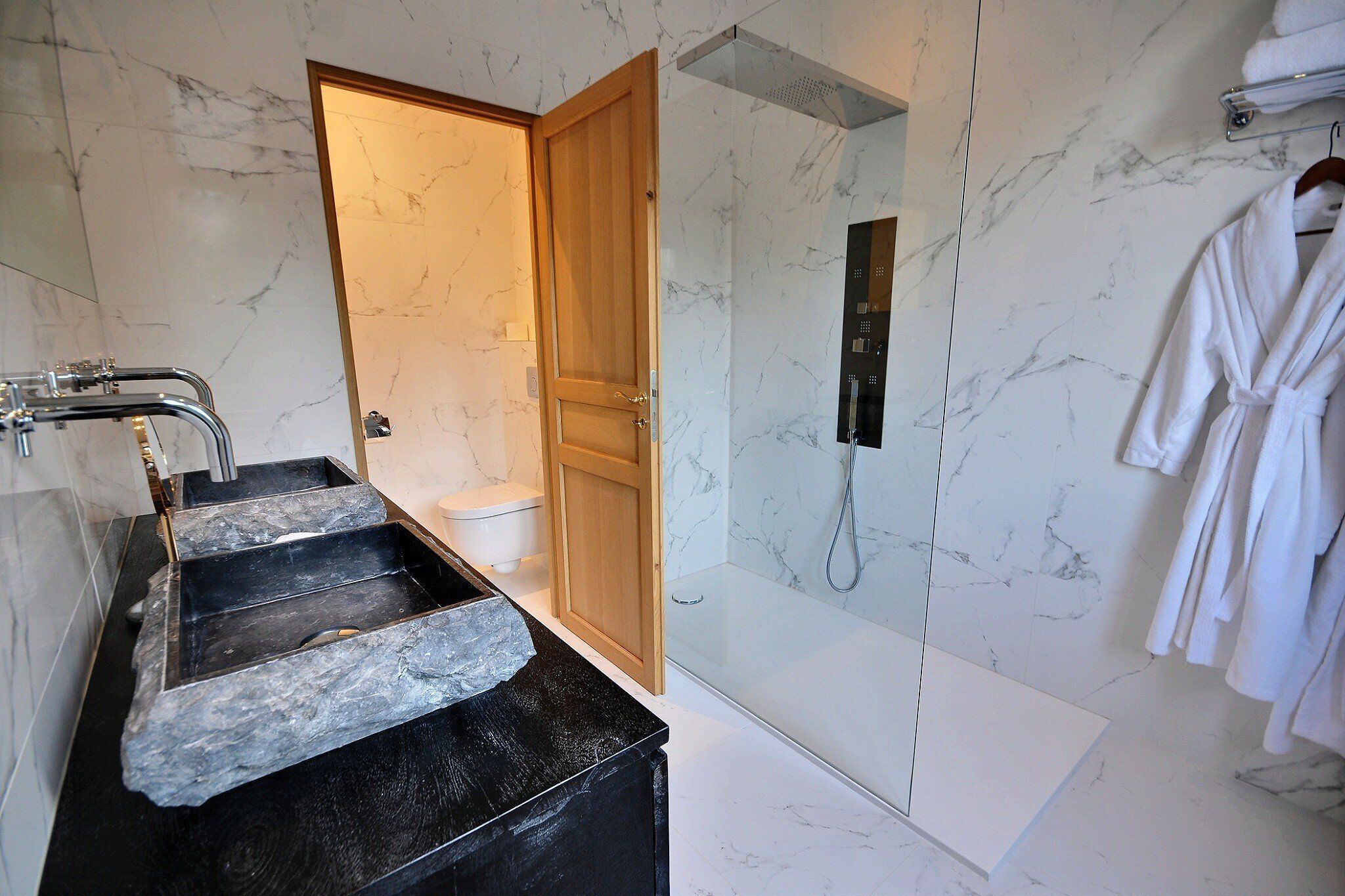 A modern bathroom with a marble sink, a shower, and a wooden door.