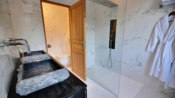 A modern bathroom with a marble sink, a shower, and a wooden door.