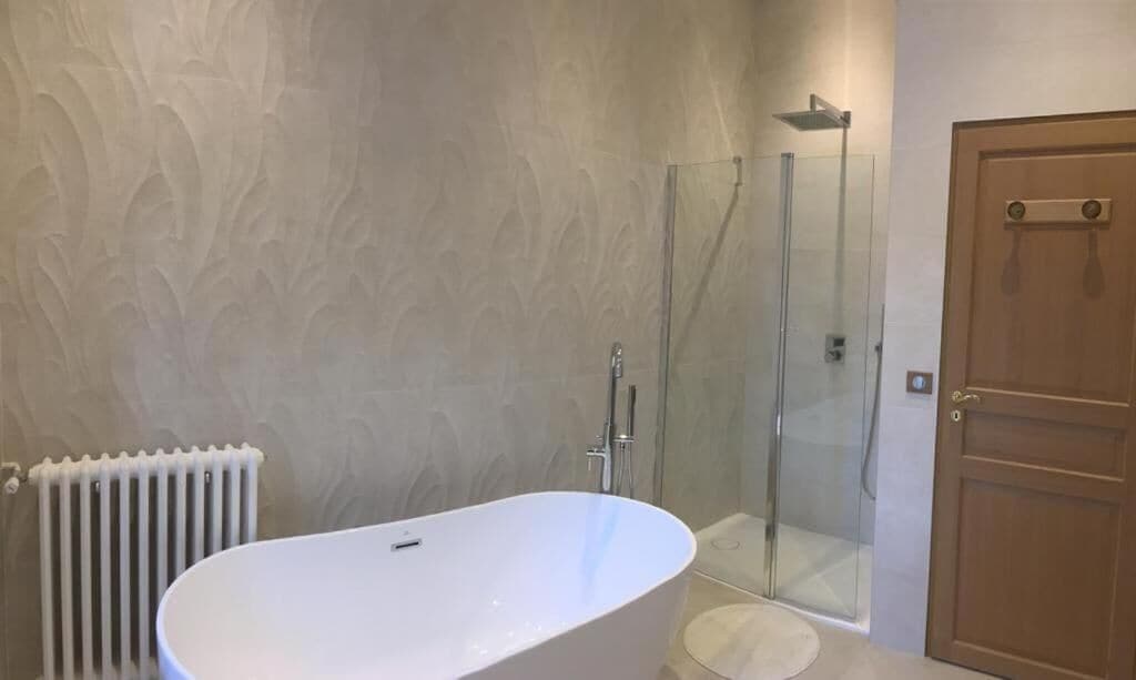 Une salle de bain avec une baignoire sur pieds, une douche à parois de verre et une porte en bois.