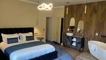 A modern hotel room with a large bed, a vanity with a mirror, and a bathtub.