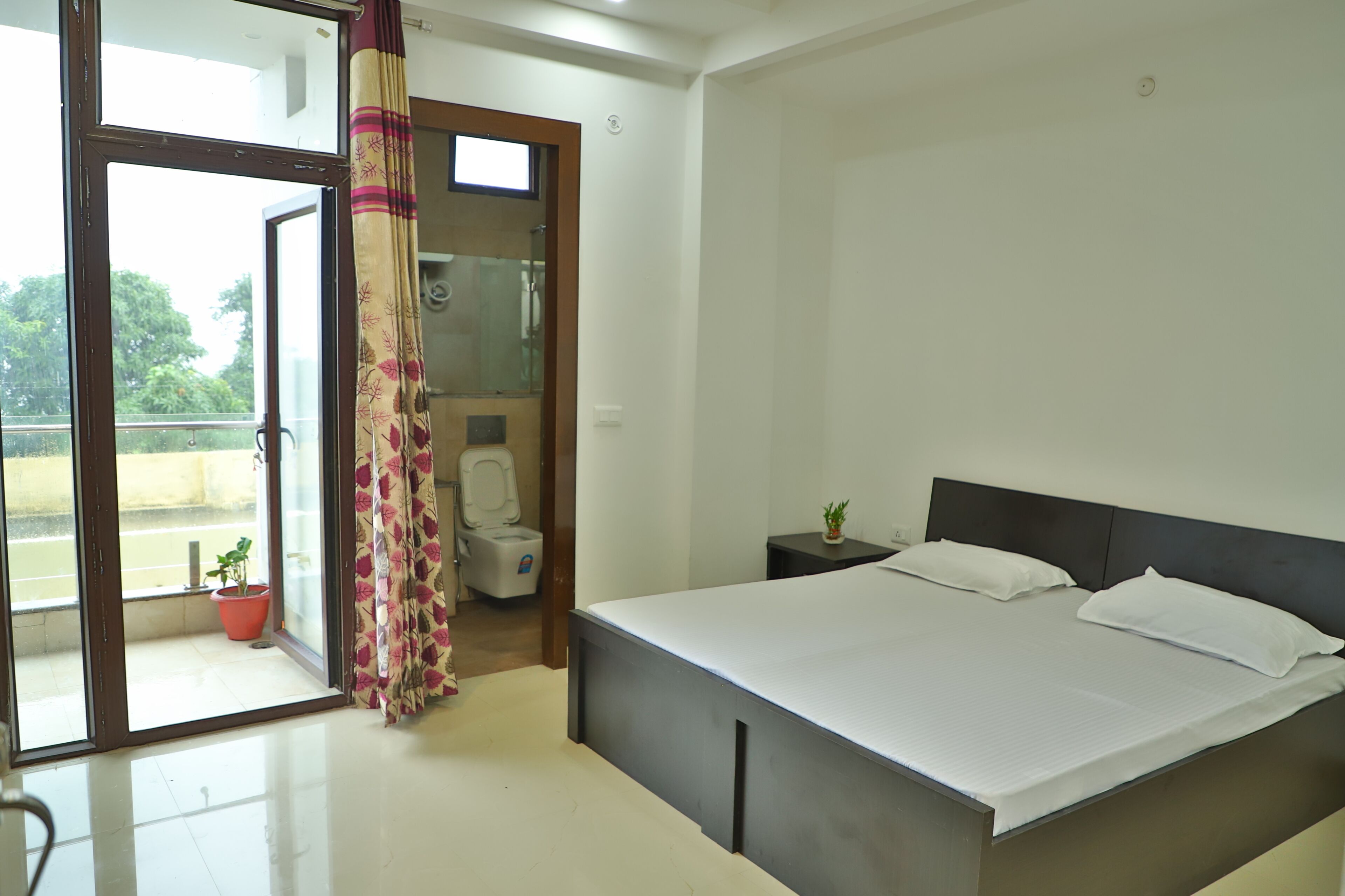 A bedroom with a bed, a nightstand, a potted plant, and a bathroom with a toilet and shower.