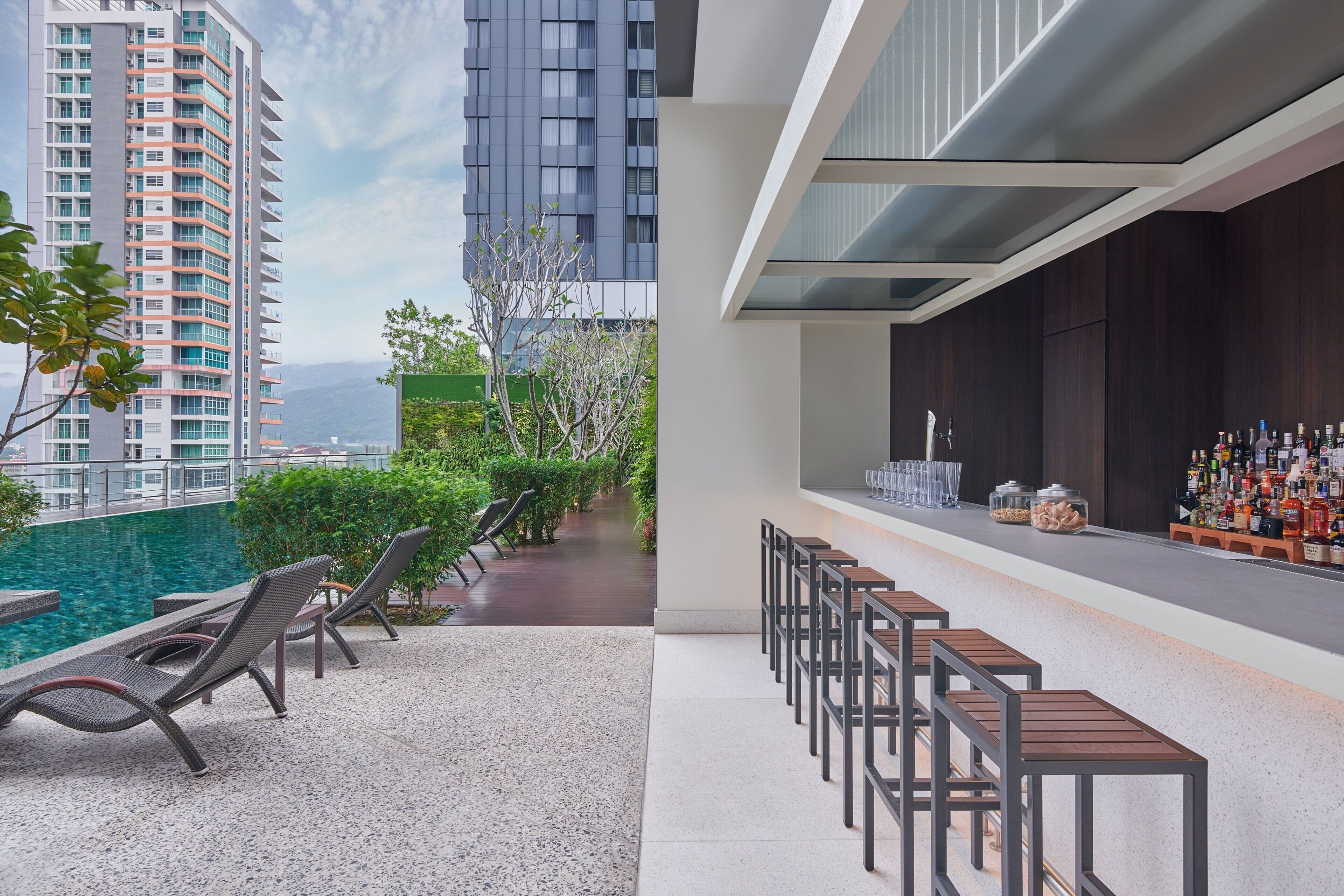A rooftop bar with lounge chairs and a poolside area, overlooking a cityscape.