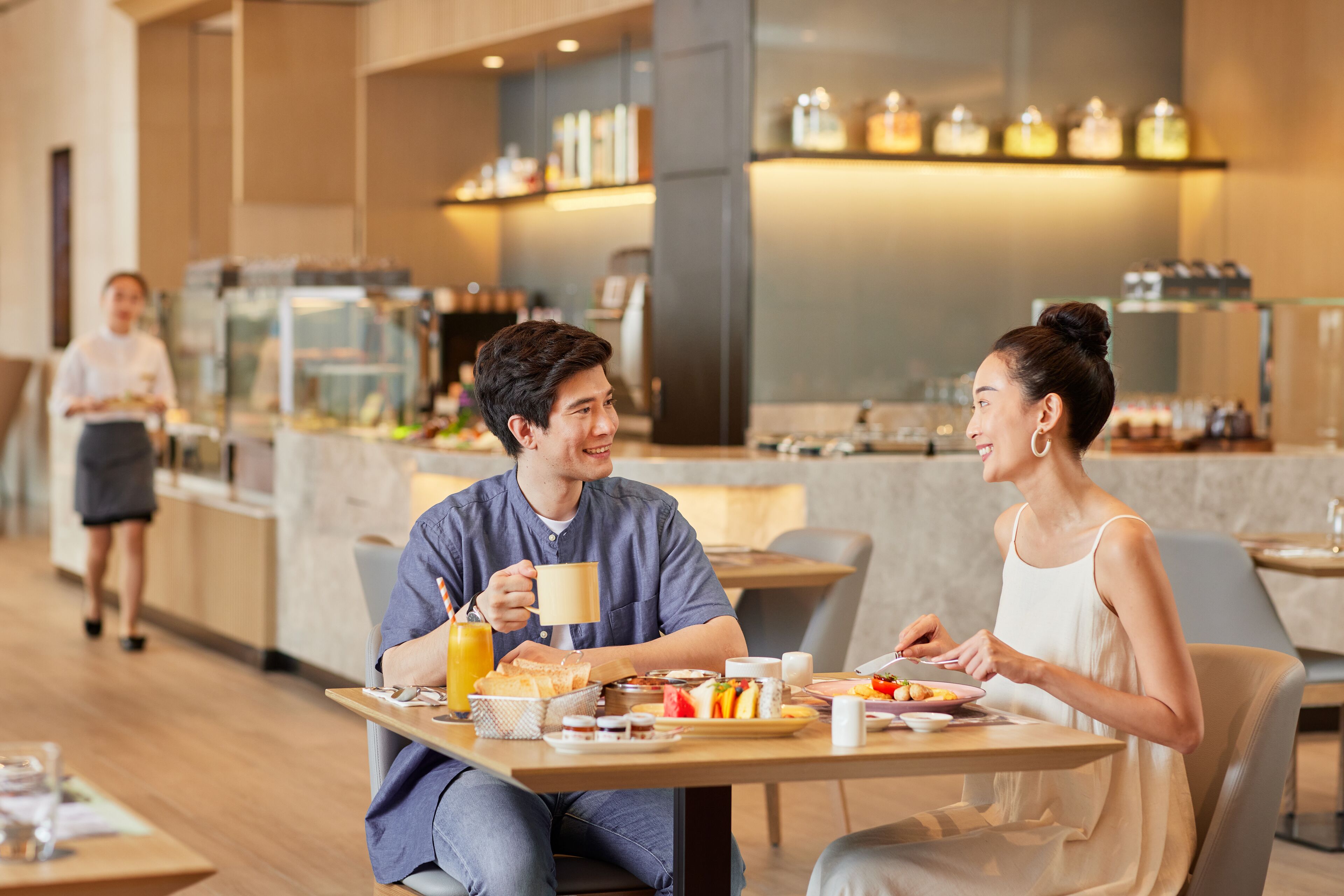 A couple dining in a modern cafe with a barista in the background.