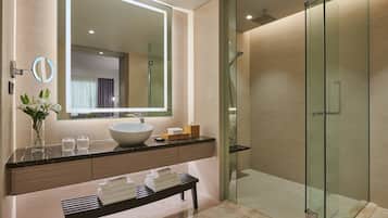 A modern bathroom with a large mirror, a vessel sink, a glass-enclosed shower, and a bench with towels.