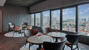 A modern interior with round tables and chairs, large windows offering a city view. - Courtyard by Marriott Penang (George Town)
