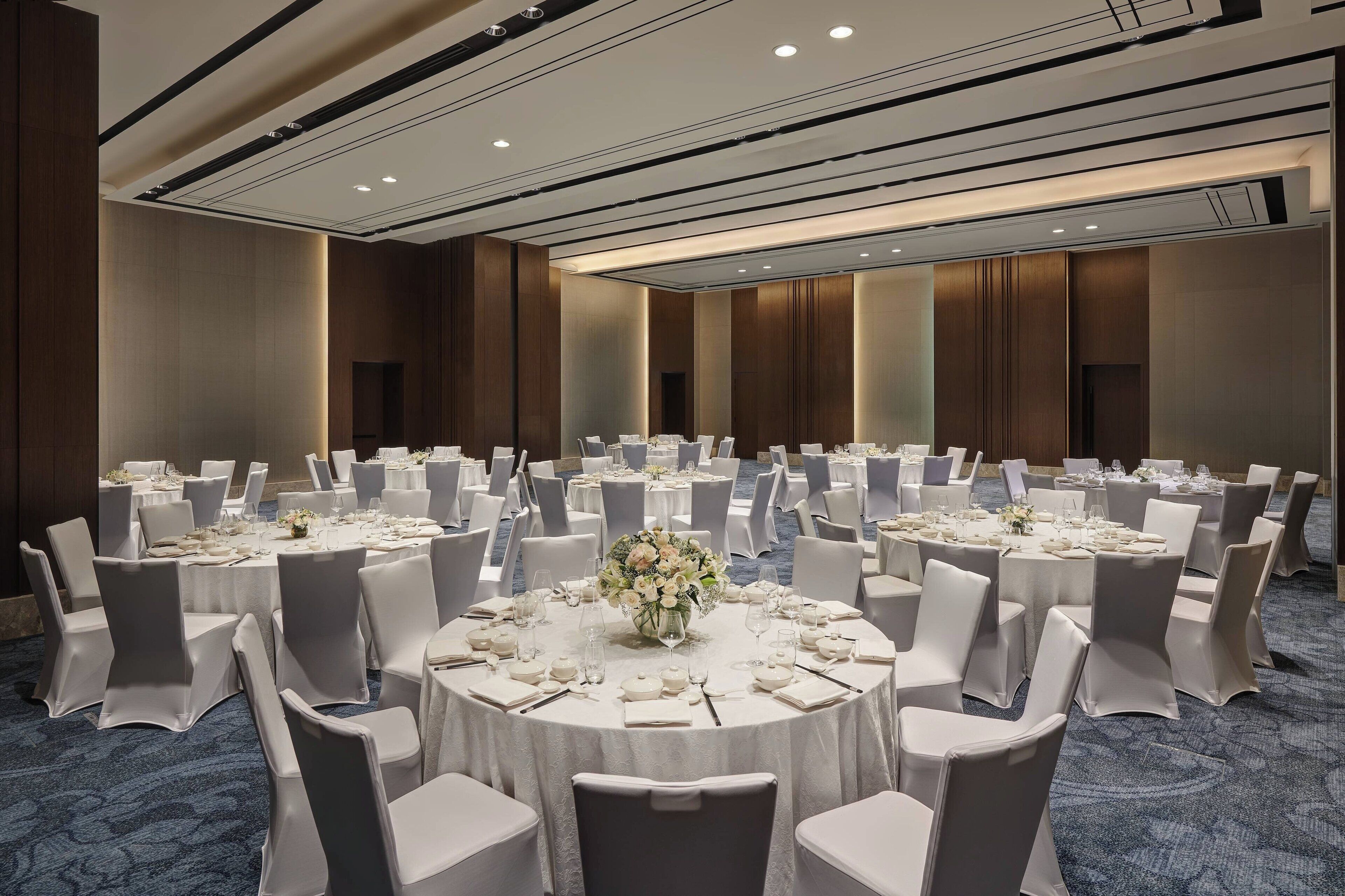 Un amplio salón de banquetes con mesas redondas dispuestas para comidas, cada una con mantel blanco y sillas.