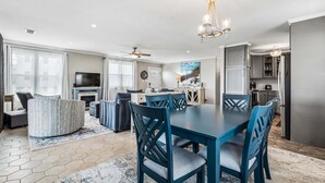 Een moderne woonkamer met een bank, eettafel en stoelen, een keuken met kastjes en een plafondventilator.