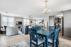 Una sala de estar moderna con sofá, mesa de comedor y sillas, una zona de cocina con armarios y un ventilador de techo.