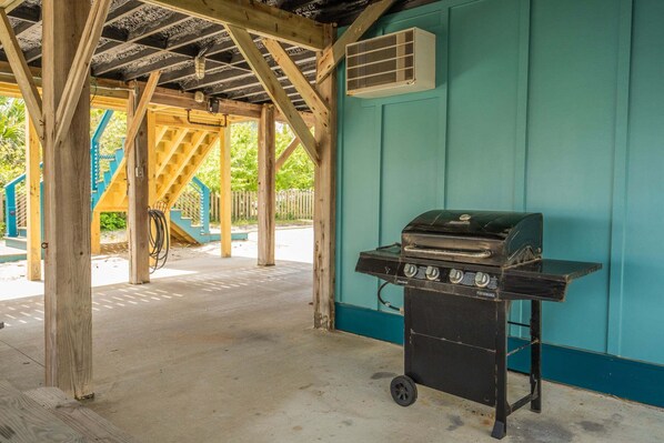 A covered outdoor area with a barbecue grill, wooden beams, and a teal wall.