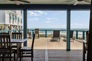 A wooden deck with outdoor seating, a view of the ocean, and a building with a balcony.
