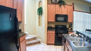 A compact kitchen with a refrigerator, microwave, stove, and sink.