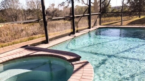 A clear swimming pool with a brick edge and a glass enclosure.