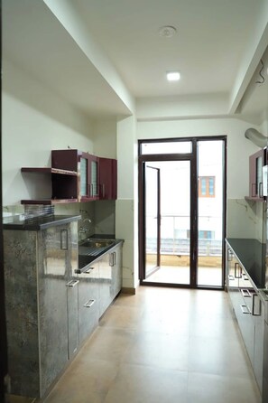 A kitchen with a central island, cabinets, and a sliding glass door leading to a balcony. - The Most Beautiful Property Of Rishikesh (Rishikesh)