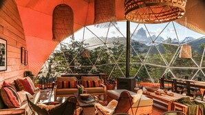 A geodesic dome interior with a wooden floor, seating area, and a large window offering a mountain view. - Chalten Camp - Glamping With A View (El Chalten)