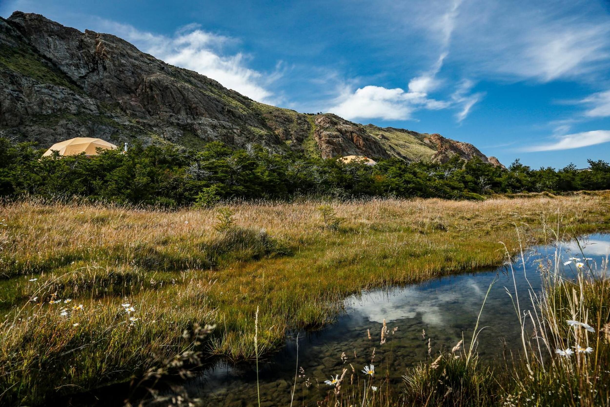 A natural landscape with a mountain, a small body of water, and a tent-like structure.