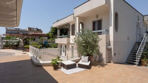 Un edificio moderno con un patio cubierto, mobiliario exterior y plantas en macetas.