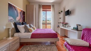 Un dormitorio con cama, mesitas de noche, televisor, escritorio y ventana con cortinas.