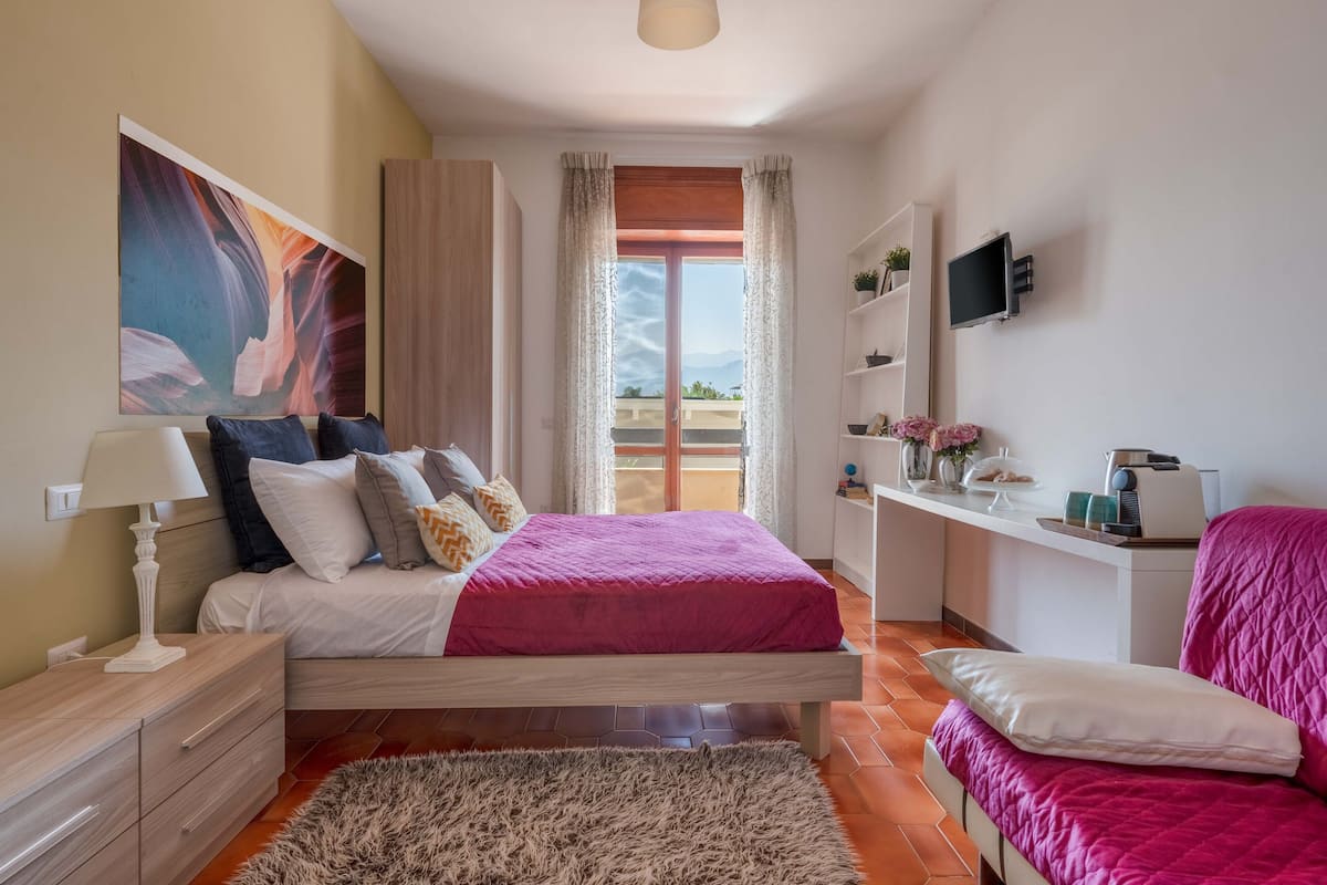 Ein Schlafzimmer mit einem Bett, Nachttischen, einem Fernseher, einem Schreibtisch und einem Fenster mit Vorhängen.
