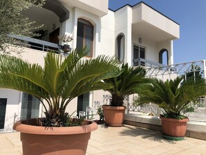 A modern building with a balcony, large terracotta planters with palm plants, and a clear blue sky. - Vera's Home Pompei (Pompei)