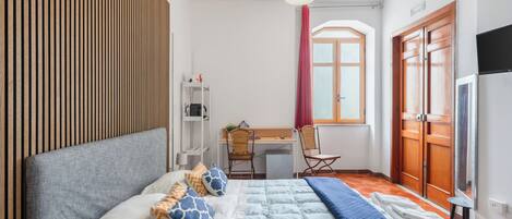 A bedroom with a bed, a desk, a chair, a TV, and a wardrobe.