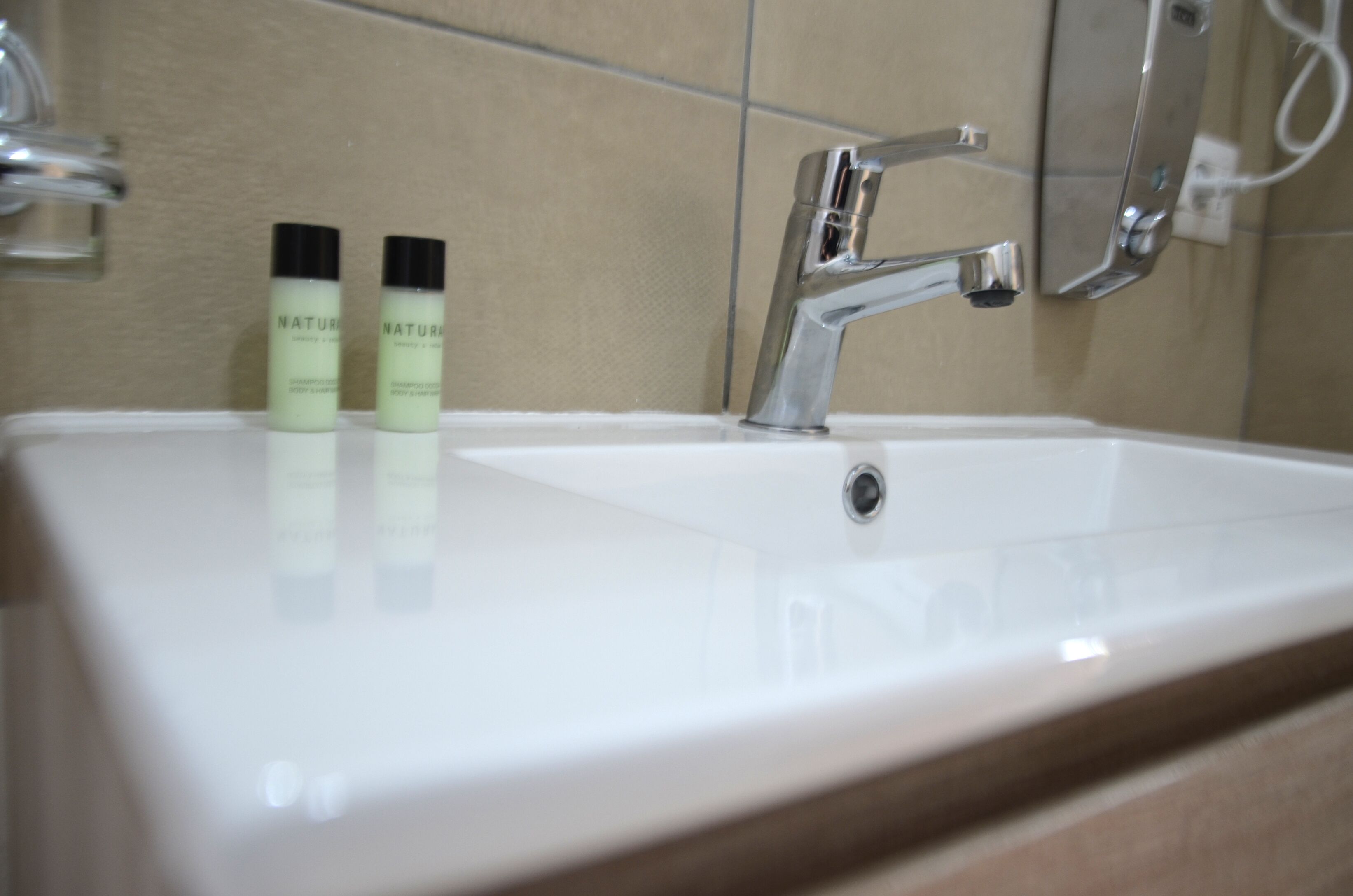 A bathroom sink with a chrome faucet, two bottles of shampoo, and a mirror.