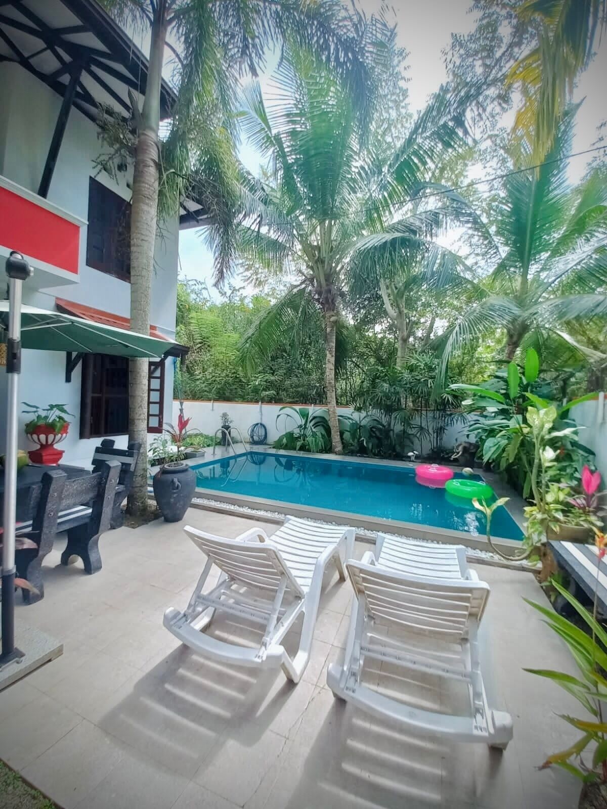 A pool area with lounge chairs, a table, and a red and white building in the background.