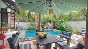 An outdoor patio area with a pool, surrounded by greenery and a large umbrella providing shade. - Luxury Villa Costanza (Hikkaduwa)